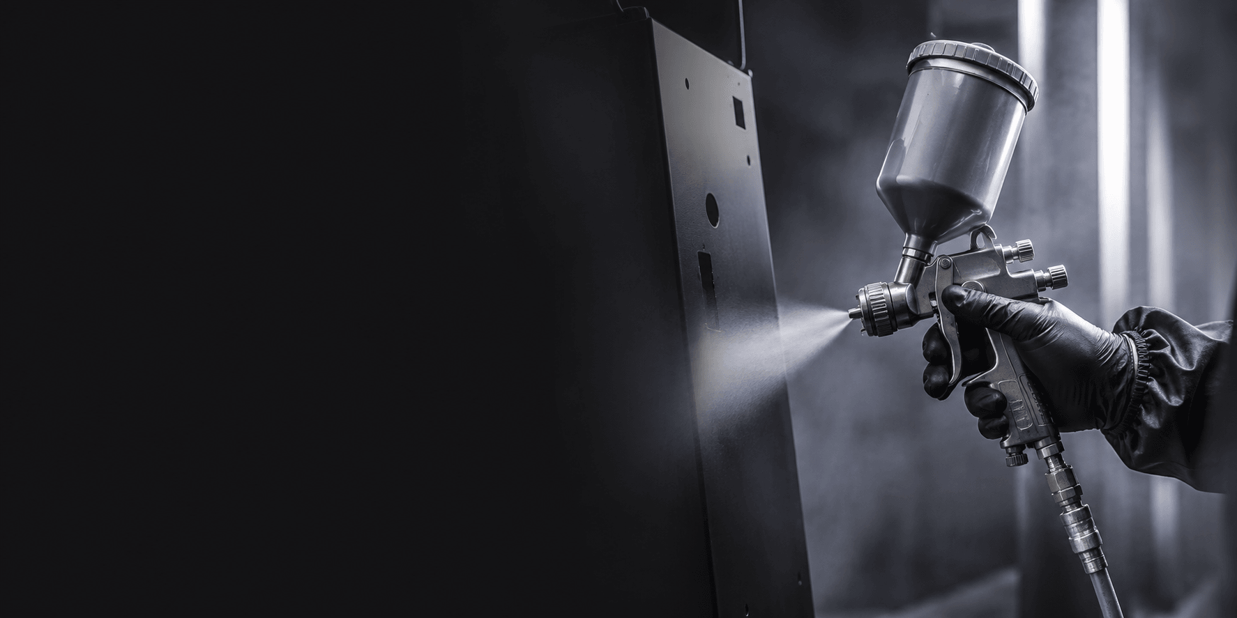 Gloved painter spraying a metal panel with an HVLP spray gun inside a finishing booth