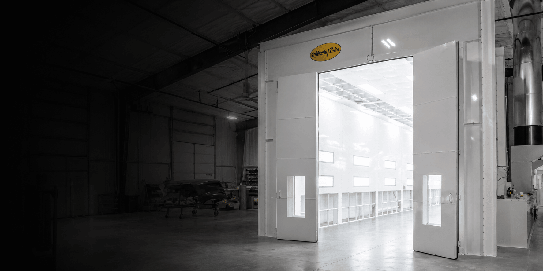 A California Pulse spray booth installed in a shop, its doors open on a brightly lit white interior