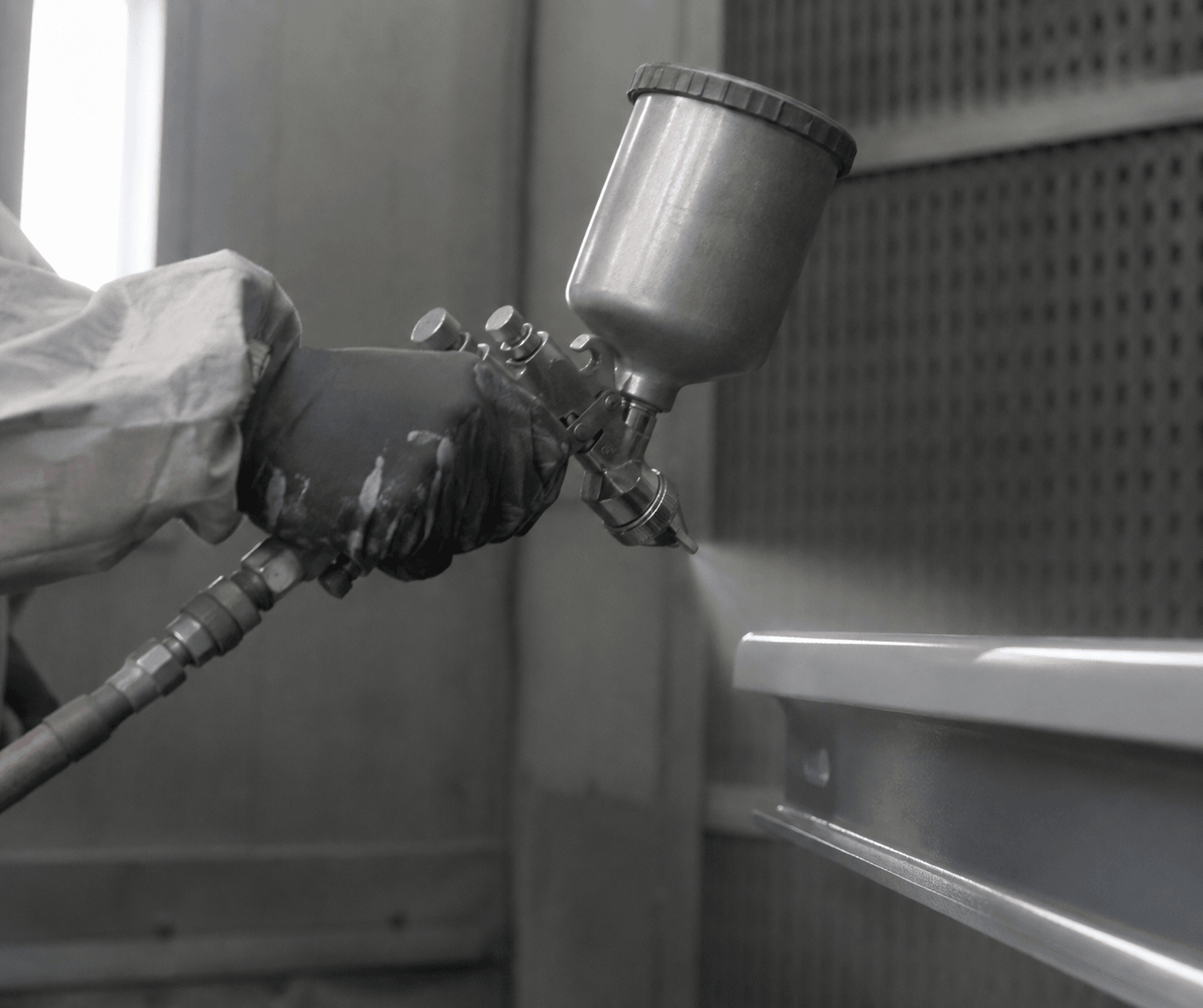 Operator spraying a coating onto a metal component inside a spray booth