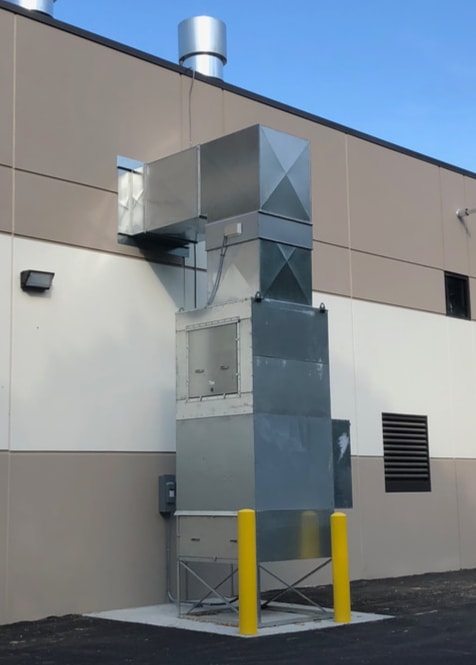 An outdoor mounted air makeup unit and exhaust stack on the side of a finishing plant