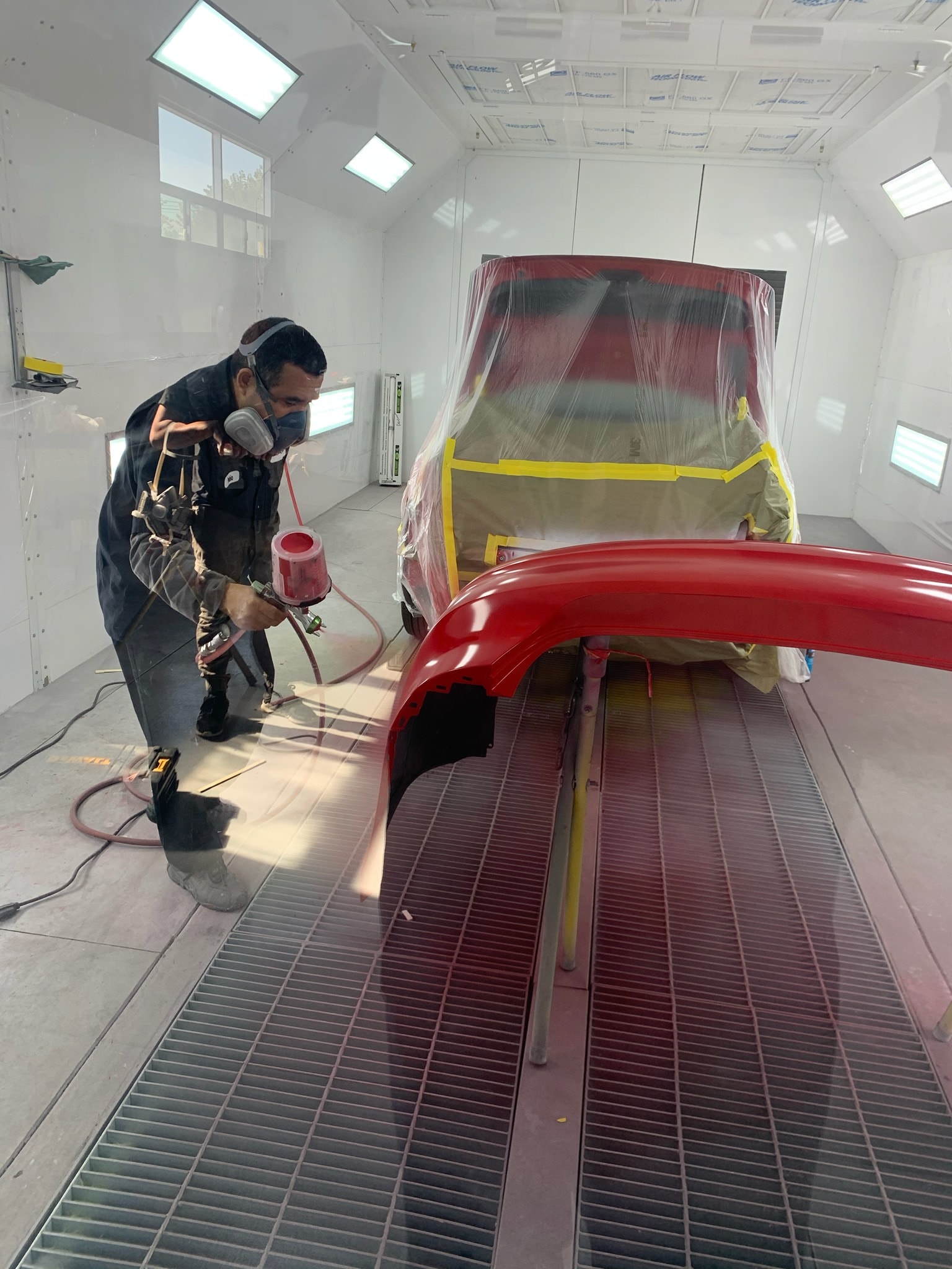 A painter spraying a red bumper inside a downdraft spray booth