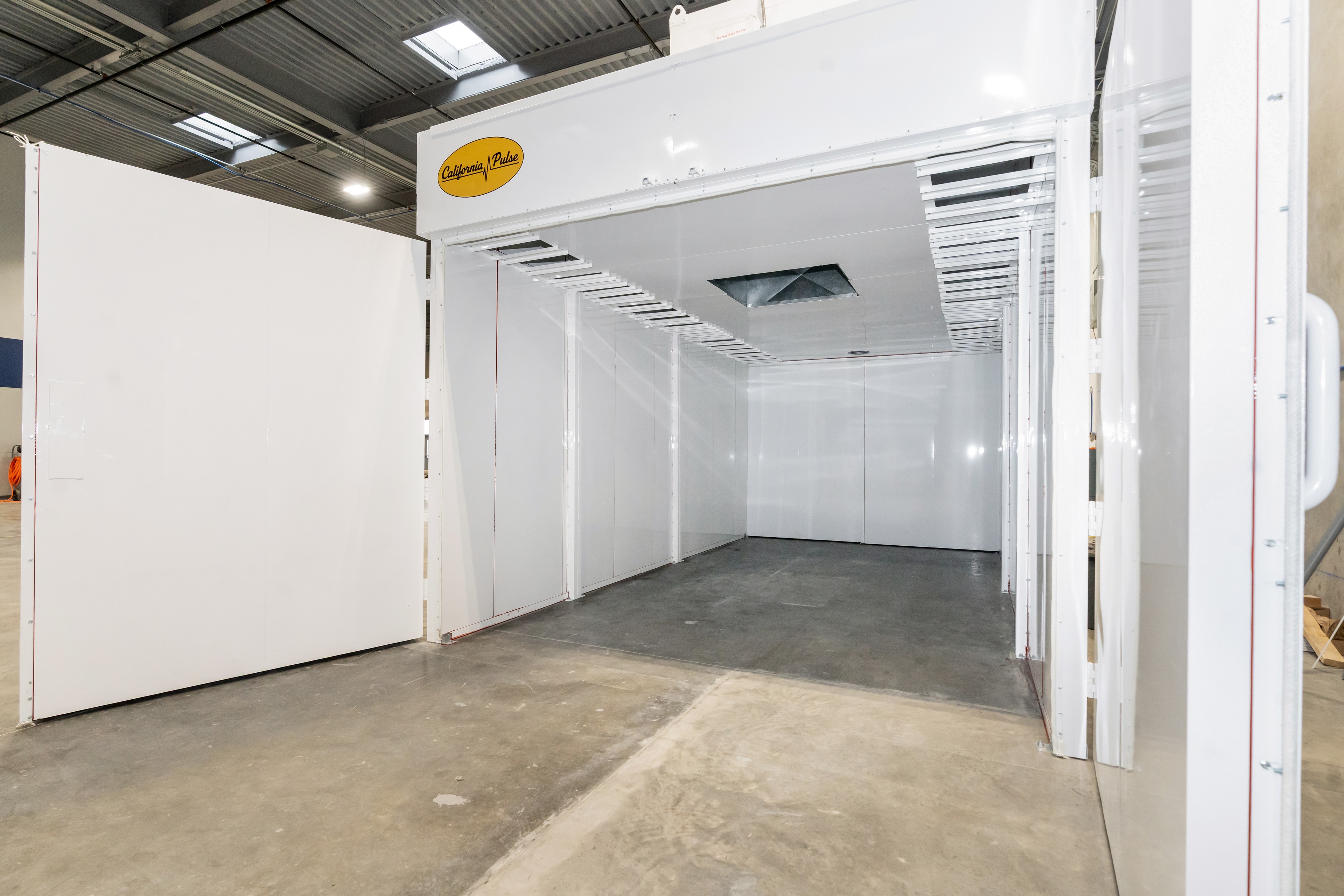 Interior of a California Pulse powder coating booth with white cleanable panels and lit openings