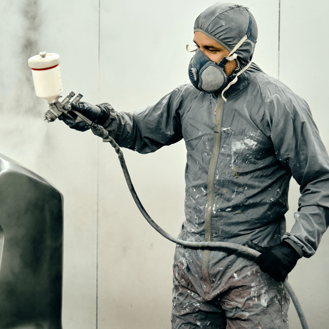 Operator in protective equipment spraying liquid coating with an HVLP gun inside a spray booth
